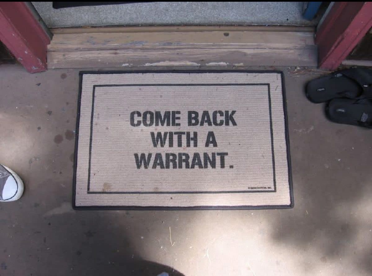 A doormat reading 'come back with a warrant' — a nod to Fourth Amendment rights